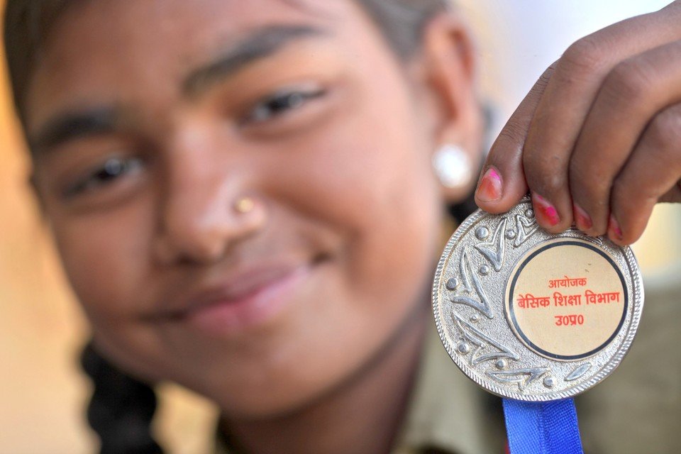 Komal, a young girl, holding up a medal she received.