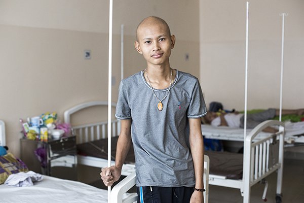A young man standing beside a bed in a hospital.